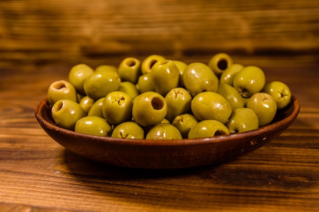 Plato de cerámica con aceitunas verdes sobre mesa de madera