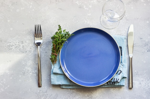 Plato de cerámica azul, servilleta de lino, cuchillo y tenedor