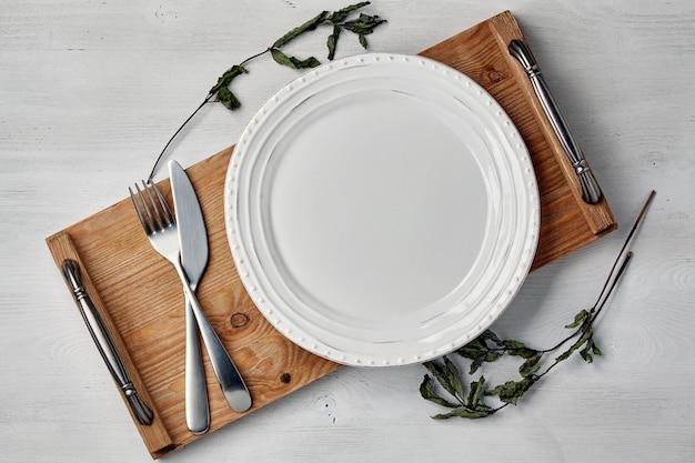 Plato de cerámica blanca y una bandeja con cubiertos y ramitas de grosellas secas