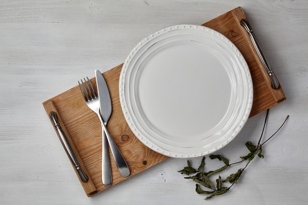 Un plato de cerámica blanca y una bandeja de cubiertos sobre una mesa de madera pintada de luz