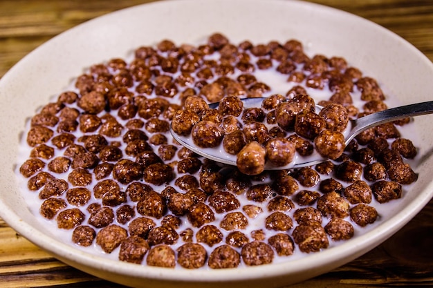 Plato de cerámica con bolas de cereal de chocolate en leche sobre mesa de madera rústica