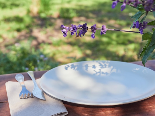 Foto plato de cerámica y cuchillo de tenedor en papel de pañuelo servido en la mesa con una planta floral