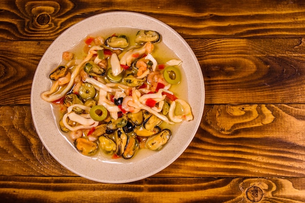 Plato de cerámica con diferentes mariscos y aceitunas en la mesa de madera Vista superior