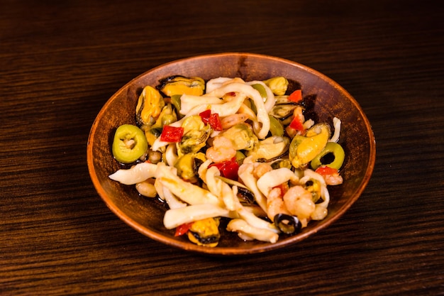 Plato de cerámica con diferentes mariscos y aceitunas sobre mesa de madera.