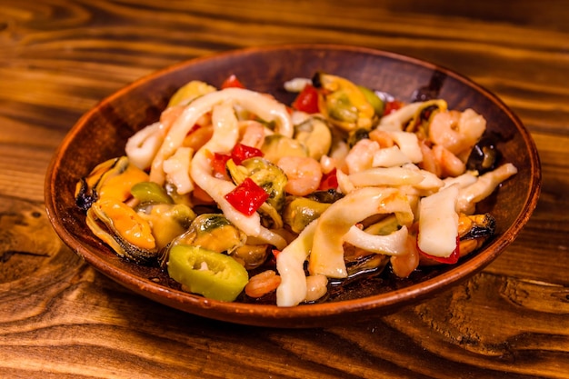 Plato de cerámica con diferentes mariscos y aceitunas sobre mesa de madera.