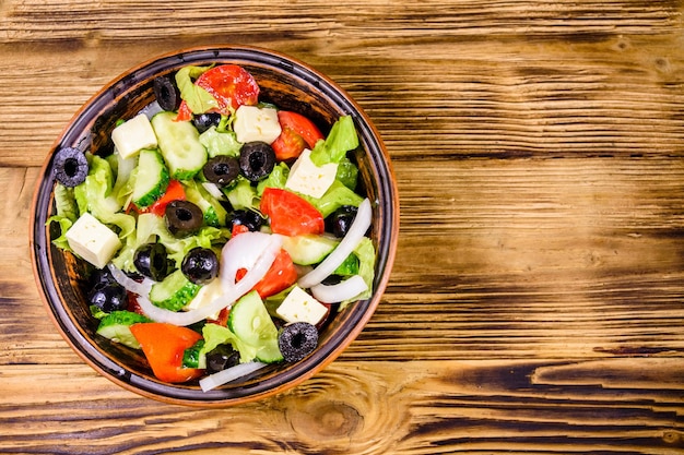 Foto plato de cerámica con ensalada griega en la mesa de madera vista superior