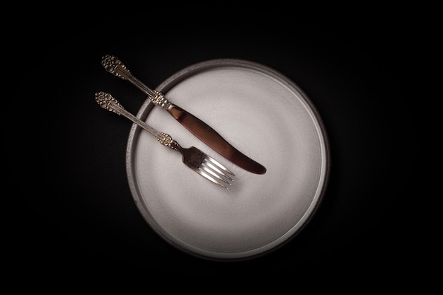 Plato de cerámica gris redondo vacío sobre fondo negro, vintage tenedor, cuchillo