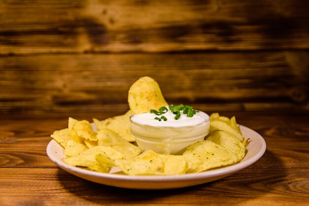 Foto plato de cerámica con papas fritas y tazón de vidrio con crema agria sobre mesa de madera