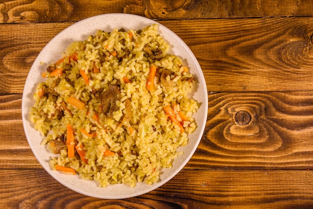 Plato de cerámica con pilaf sobre mesa de madera rústica. Vista superior