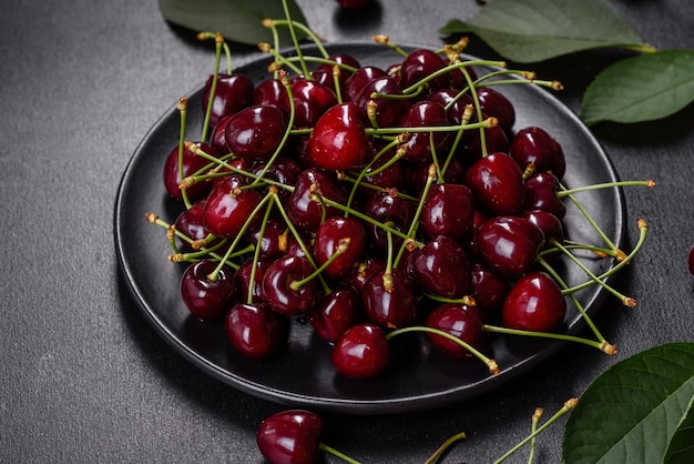 Plato de cerezas dulces frescas con hojas en gotas de agua en la vista superior de fondo de piedra