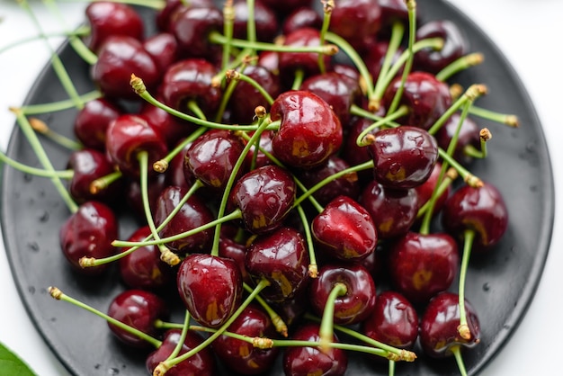 Plato de cerezas dulces frescas con hojas en gotas de agua en la vista superior de fondo de piedra