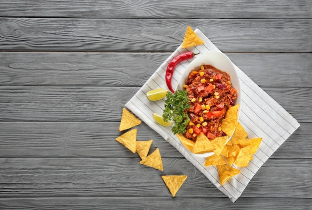 Plato con chili con carne y chips de nacho sobre fondo de madera