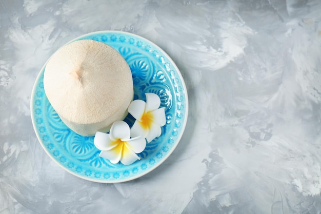 Plato con coco fresco y hermosas flores sobre fondo de textura gris