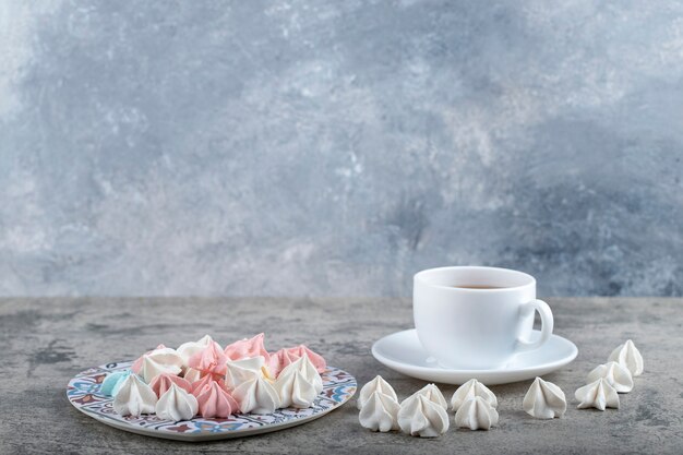 Plato de coloridos caramelos de merengue dulce y taza de té sobre fondo de piedra.