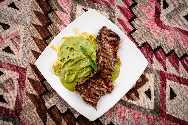 Plato de comida con carne asada y fideos verdes en una mesa artesanal
