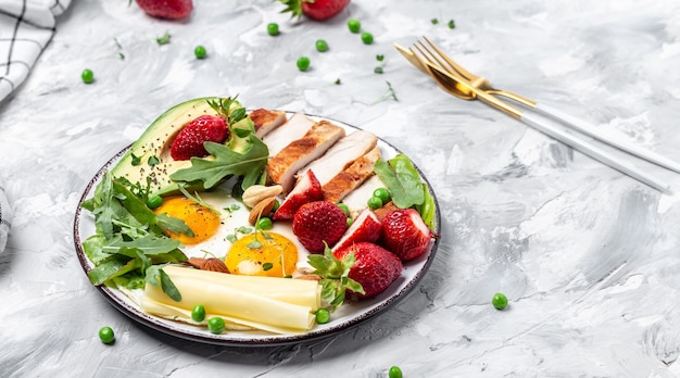 Plato con comida de dieta cetogénica. Desayuno keto Huevo frito, aguacate, fresa, filete de pollo a la plancha, queso, nueces y rúcula, dieta cetogénica. Concepto de comida sana, vista superior