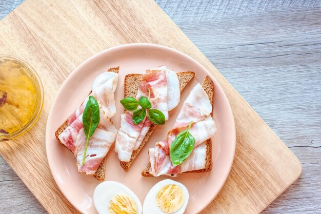 Plato de comida con sándwiches y huevos Pan con rebanada de tocino y albahaca Aceite de oliva aromático con pimienta