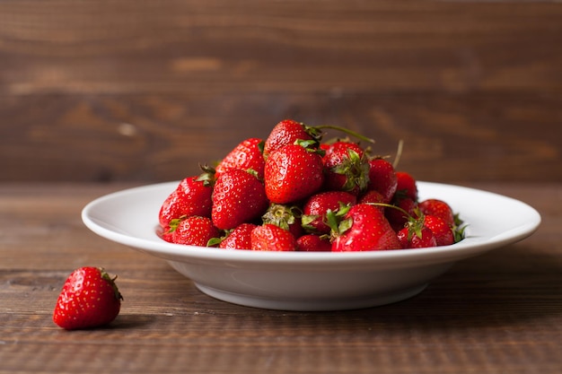 Plato completo de fresas frescas maduras y una fresa en la mesa de madera