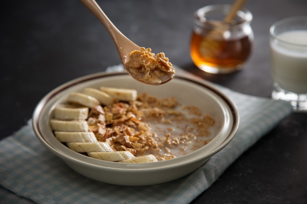 Plato con copos de avena integral con frutos de plátano, mano humana con cuchara