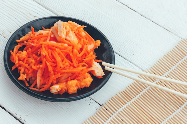 Plato coreano de zanahorias y peces rojos y palillos sobre fondo de madera blanco