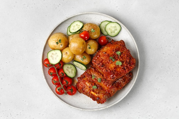 Plato con costillas a la barbacoa de cerdo marinadas patatas jóvenes tomates sobre fondo gris Vista superior