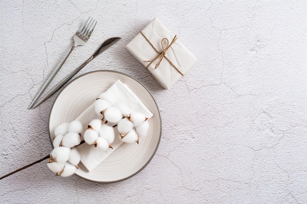 Plato cubiertos de regalo y rama de algodón sobre un fondo gris texturizado Servicio ecológico Vista superior