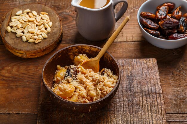 Un plato de cuscús con azafrán y nueces en una mesa de madera junto a dátiles y nueces guardan un lugar