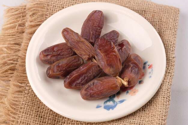 Un plato de dátiles en un paño de arpillera dátiles acechados en un plato de cerámica blanca Platos iftar de Ramadán