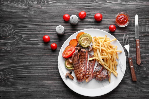 Plato con delicioso bistec a la parrilla y guarnición en mesa de madera