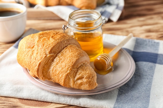 Plato con delicioso croissant fresco y tarro de miel sobre mesa de madera