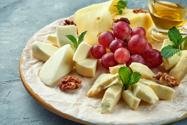 Un plato de diferentes quesos acompañado de uvas, frutos secos y miel. Plato de queso de aperitivo. Camembert en rodajas, queso brie, queso azul parmesano