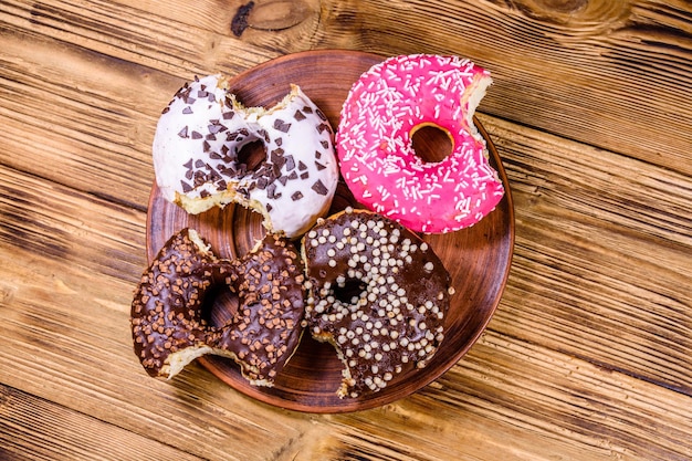 Plato con donuts glaseados mordidos en una mesa de madera Vista superior