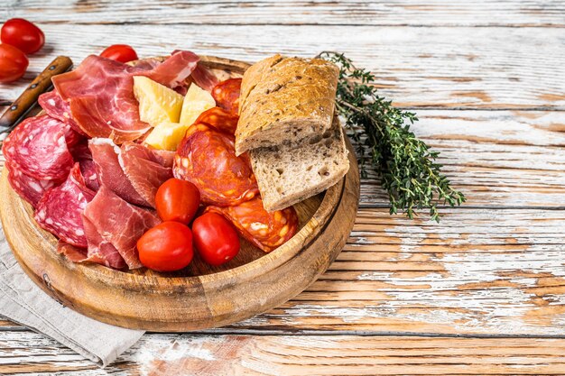 Plato de embutidos, embutidos tradicionales tapas españolas sobre una tabla de madera. Fondo de madera blanca. Vista superior. Copie el espacio.