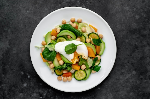 Un plato de ensalada de aguacate, garbanzos, calabaza, pepino, huevo escalfado en un plato