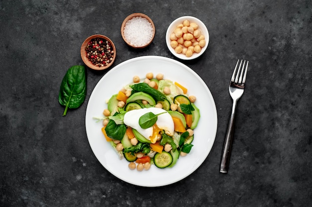 Un plato de ensalada de aguacate, garbanzos, calabaza, pepino, huevo escalfado en un plato