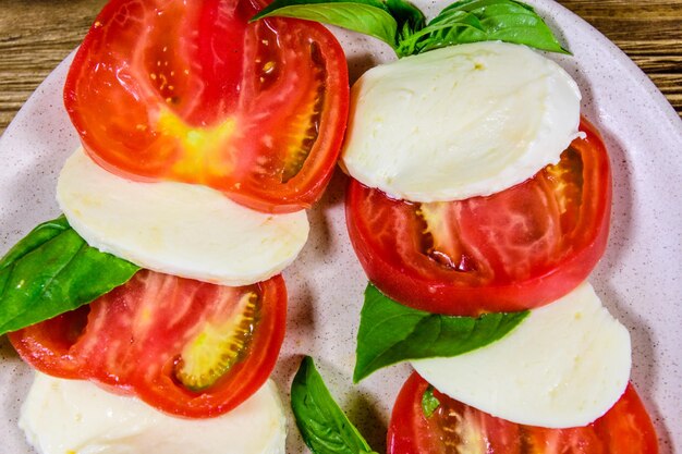 Plato con ensalada caprese ensalada italiana con tomates cherry queso mozzarella y hojas de albahaca sobre mesa de madera Vista superior