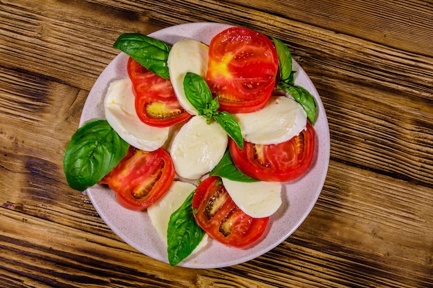 Plato con ensalada caprese ensalada italiana con tomates cherry queso mozzarella y hojas de albahaca sobre mesa de madera Vista superior