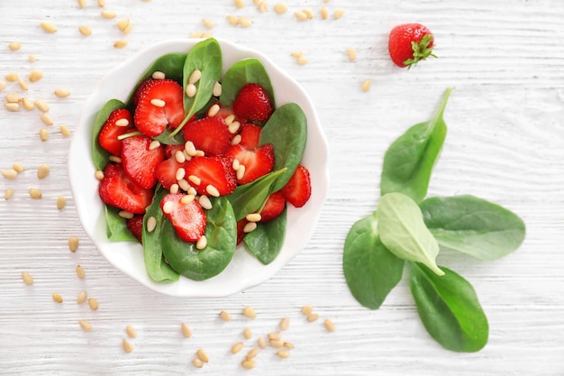 Plato de ensalada con espinacas, fresas y piñones en la mesa