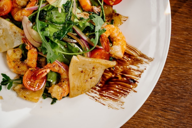 Plato de ensalada fresca con camarones, tomate y verduras mixtas en la superficie de madera de cerca