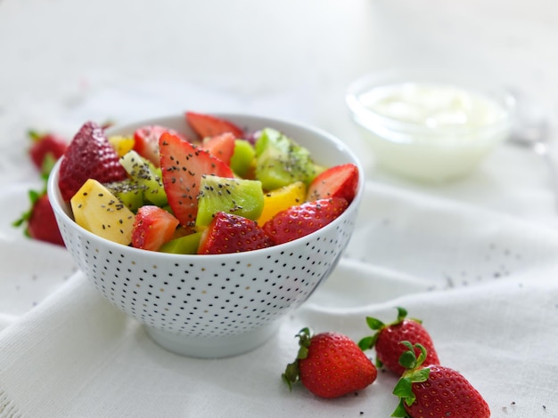 Un plato de ensalada de frutas con fresas y kiwis sobre un mantel blanco.