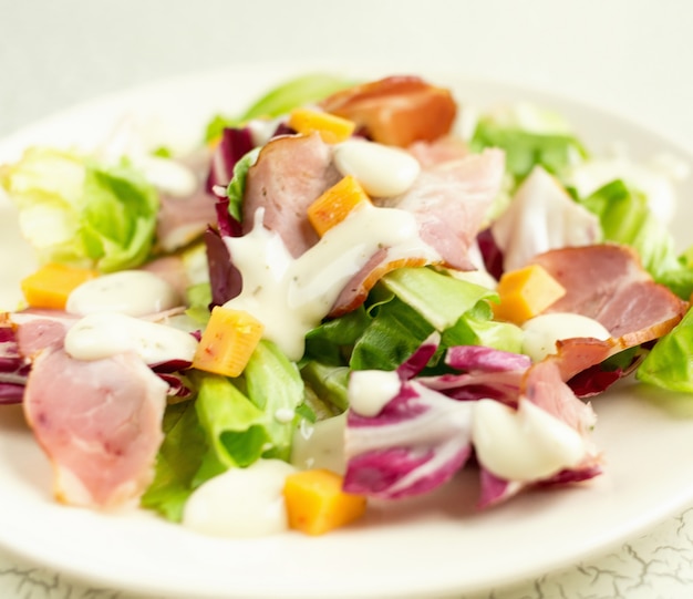 Plato de ensalada con hojas verdes, jamón, queso y salsa blanca