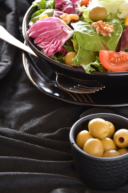 Plato de ensalada con lechuga, tomate, aceitunas y aceite. Sobre un paño negro