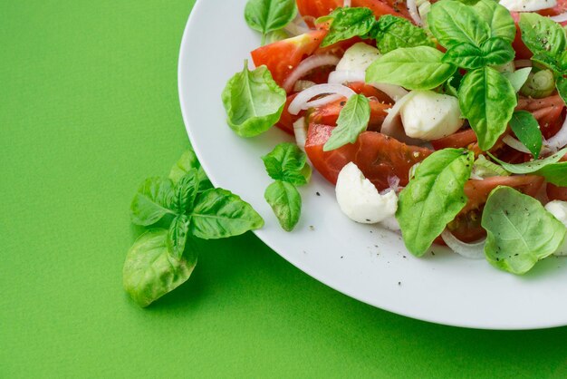 Un plato de ensalada con queso mozzarella, tomates frescos y hojas de albahaca