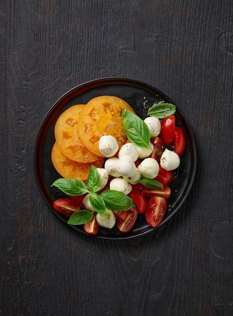 Plato de ensalada de tomate y mozzarella en la mesa de la cocina de madera negra, vista superior