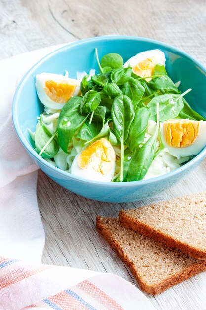 Un plato de ensalada y un trozo de pan de centeno sobre un fondo de madera Espinacas, albahaca, repollo y huevos Comida