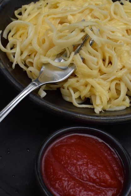 Un plato de espagueti con un pequeño plato de ketchup al lado.