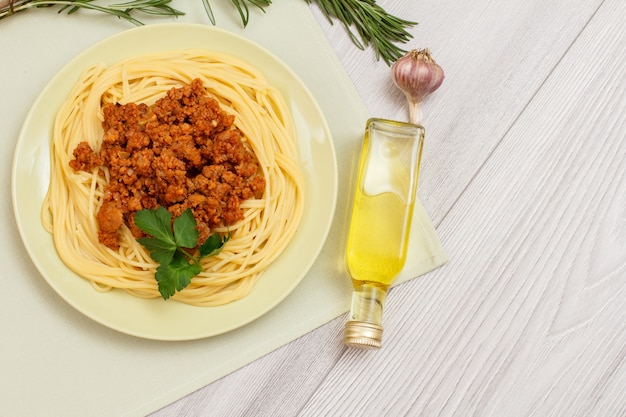 Plato con espaguetis a la boloñesa e ingredientes para cocinar. Botella de vidrio de aceite, ajo y romero. Vista superior.