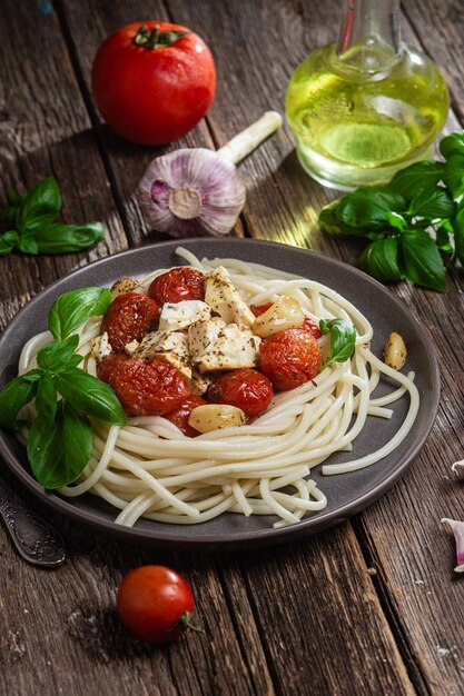 Un plato de espaguetis con tomates, queso feta y albahaca sobre una mesa de madera.