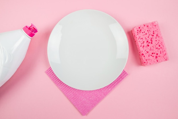 Plato de esponja blanco vacío y botella de detergente para platos sobre fondo rosa Vista desde arriba