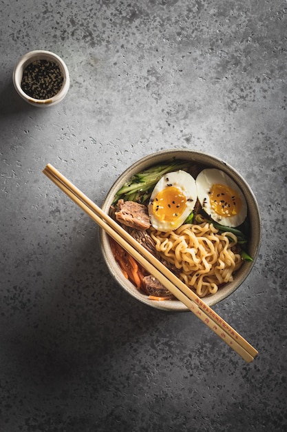 Foto un plato de fideos chinos, carne, huevo, zanahorias y cebollas se asienta sobre una mesa de hormigón gris minimalismo